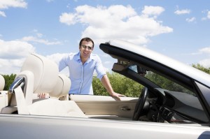 Smiling man and a cabriolet car against blue sky.